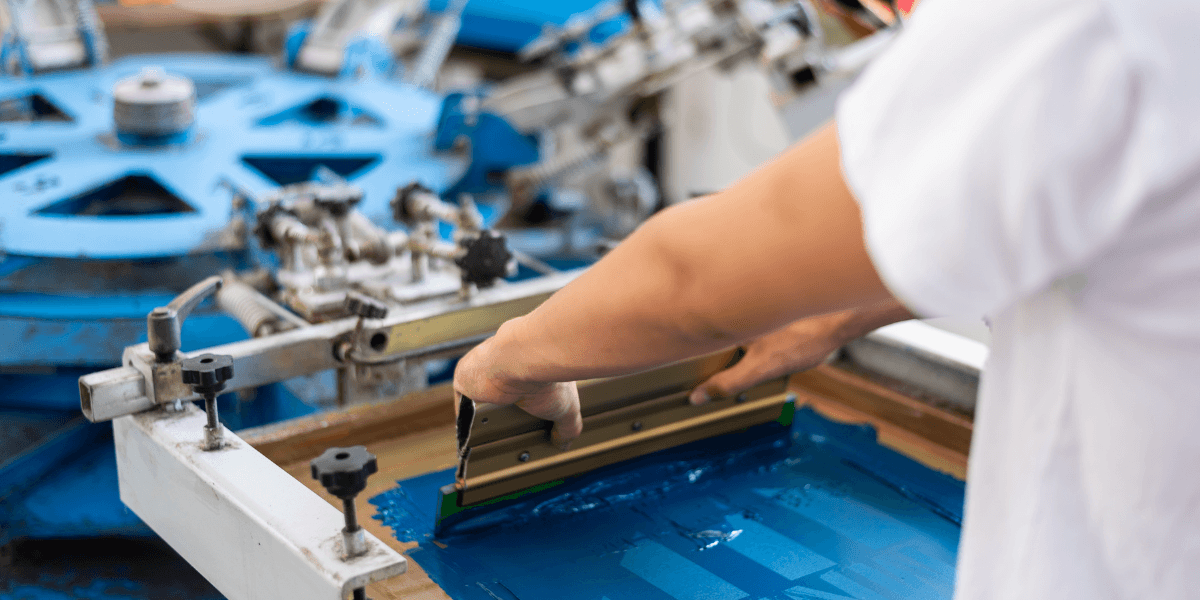 Custom screen printing process applying blue ink to apparel using a professional screen printing press